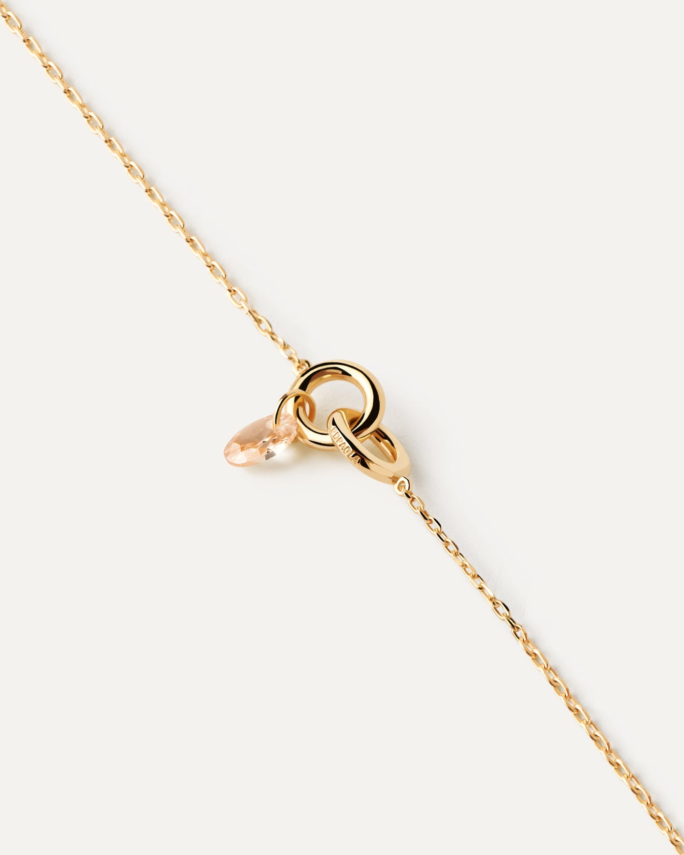 Gold-plated bracelet featuring two interlinked rings with a peach zirconia drop pendant